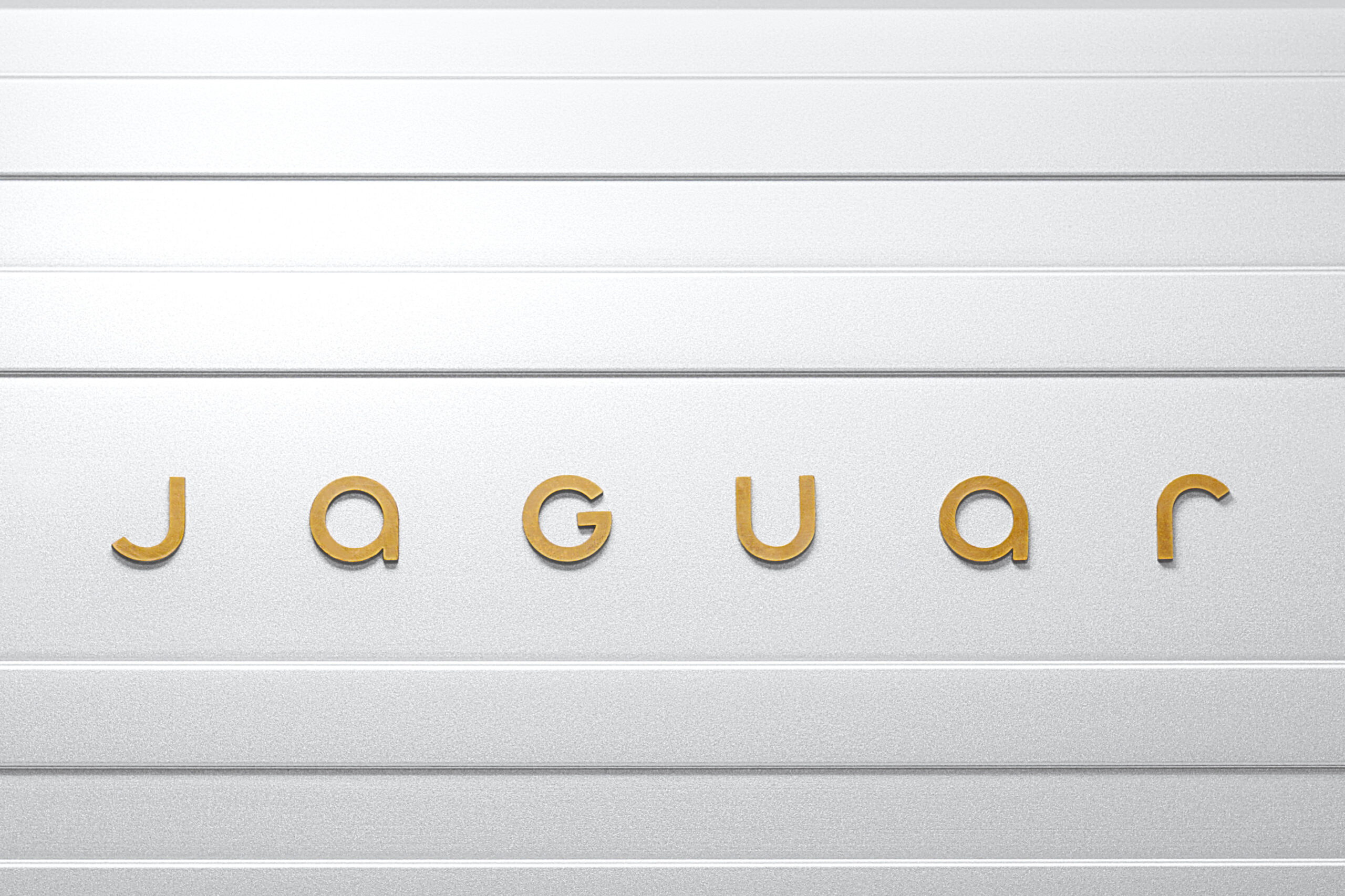 New Jaguar JaGUar device mark — mixed-case letterforms in brass on the brand's strikethrough panel